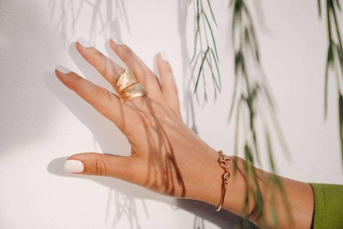 Hand mit weiss-lackierten Nägel, Fingerring und Armband aus Gold.